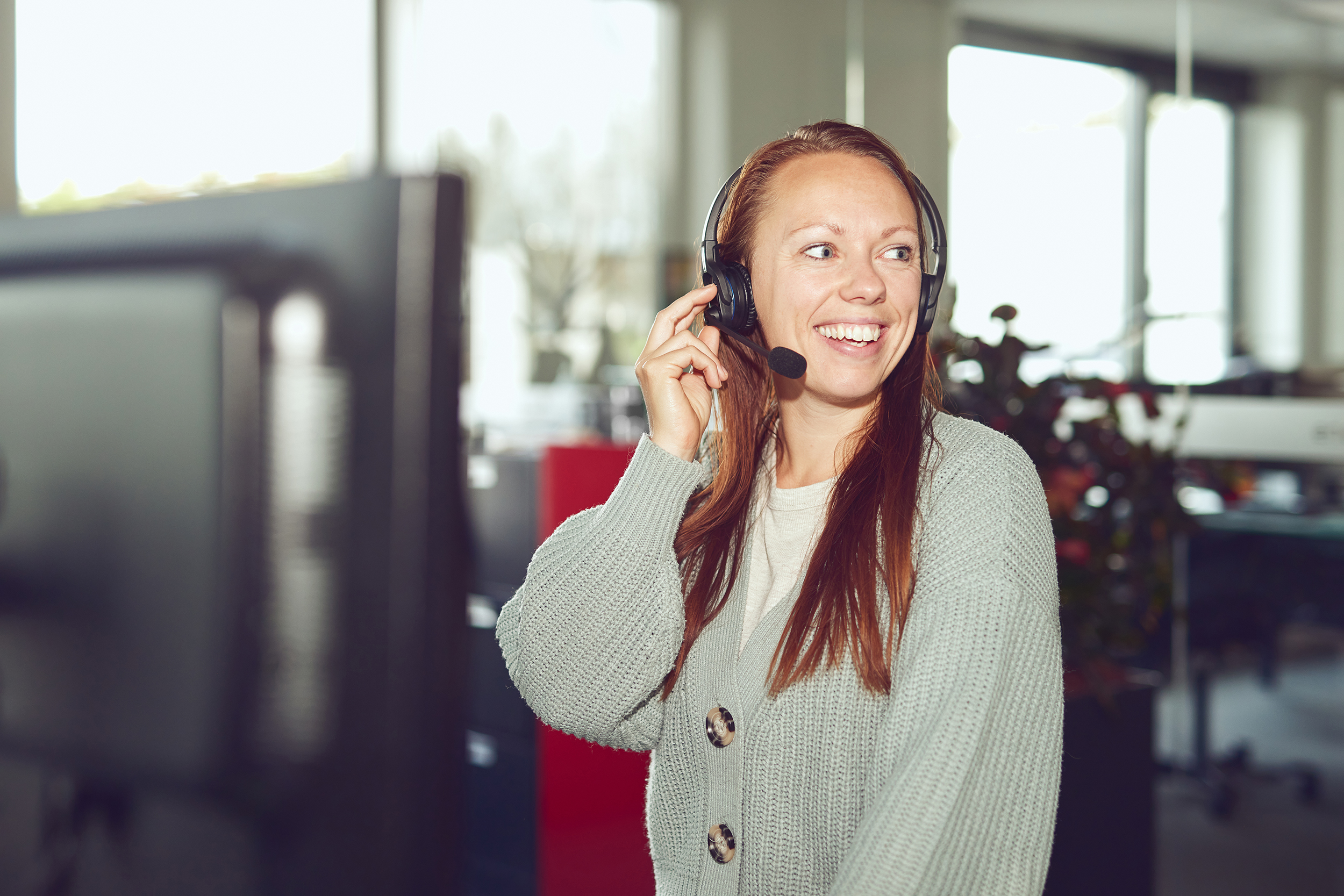 Smilende kundeservicemedarbejder i receptionen taler med kunde i headset